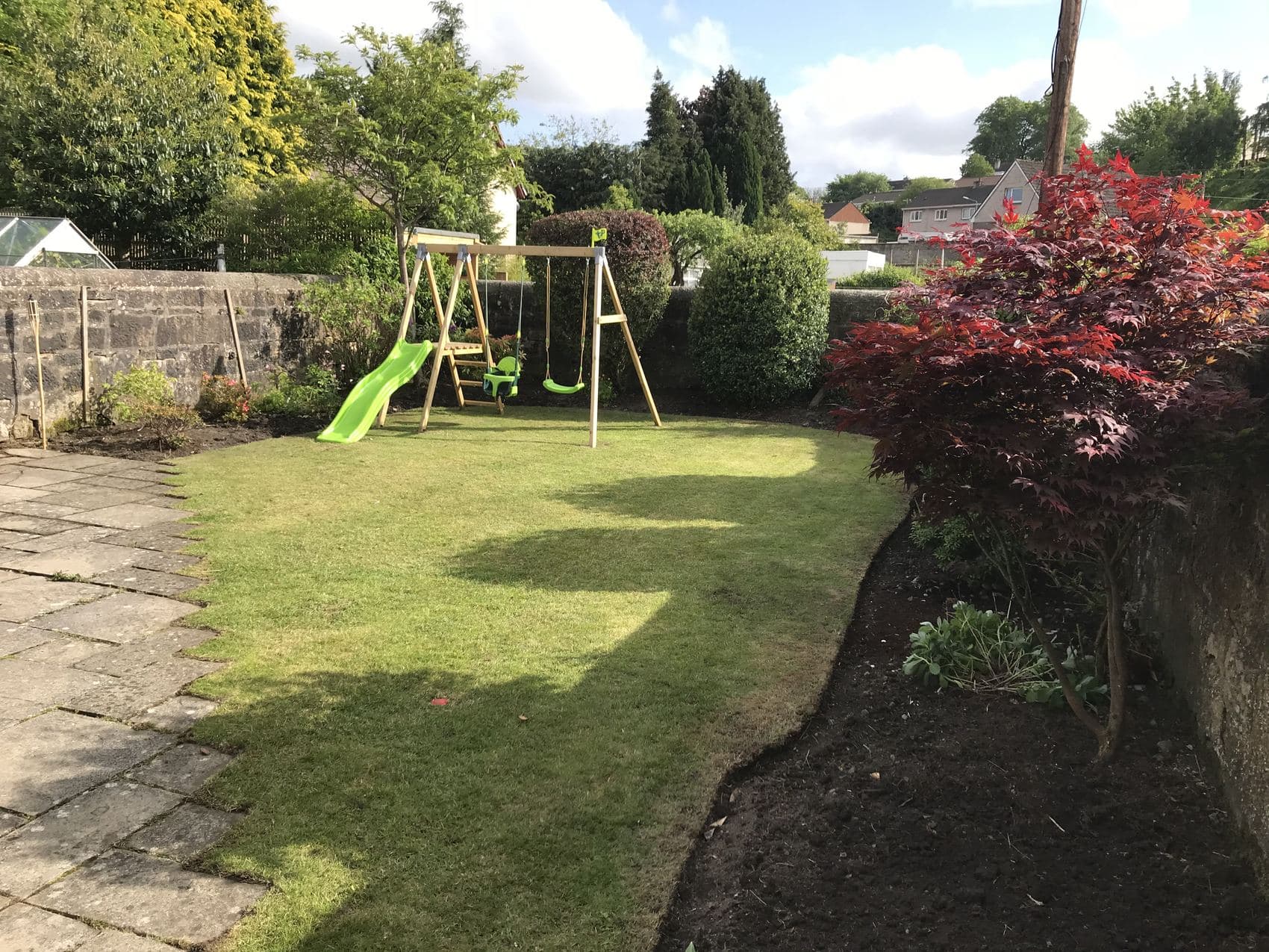 Family garden with a mown lawn, swing set, paved path and a mature red acer