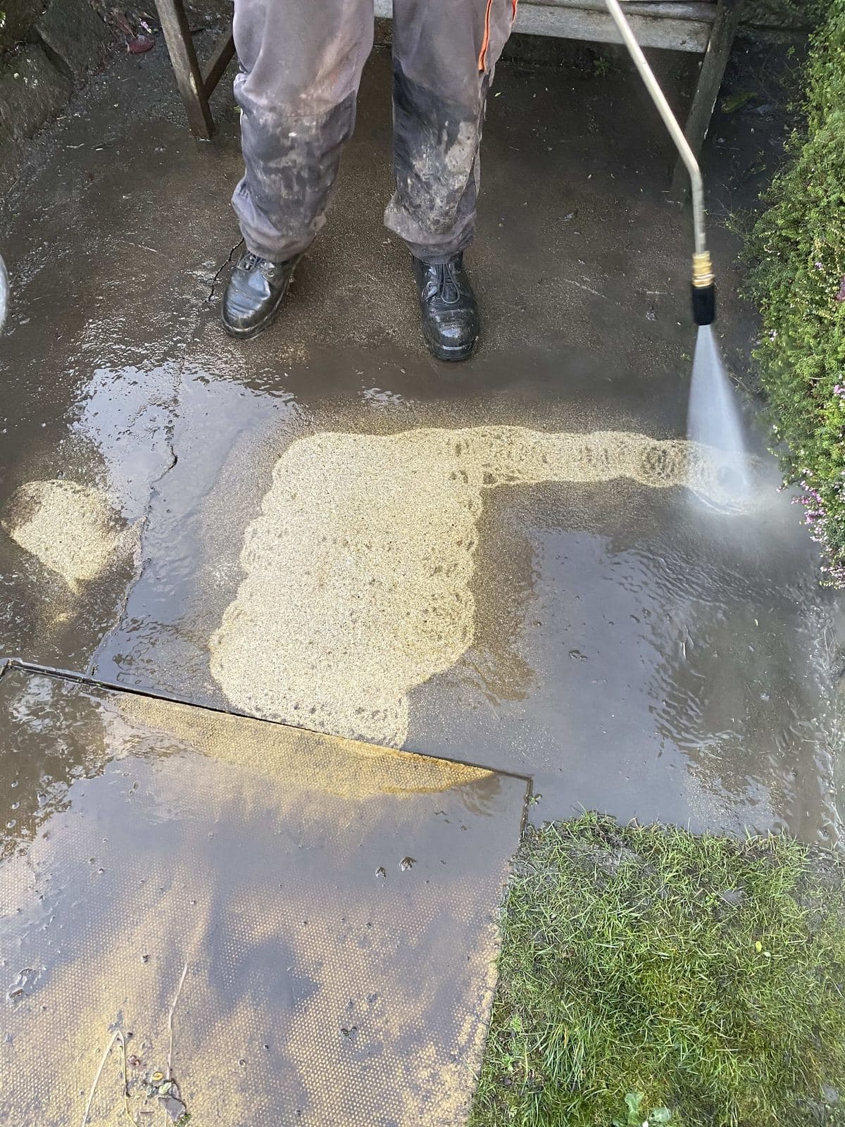 Pressure washing a paved patio, showing the cleaned slab against the dirty ones