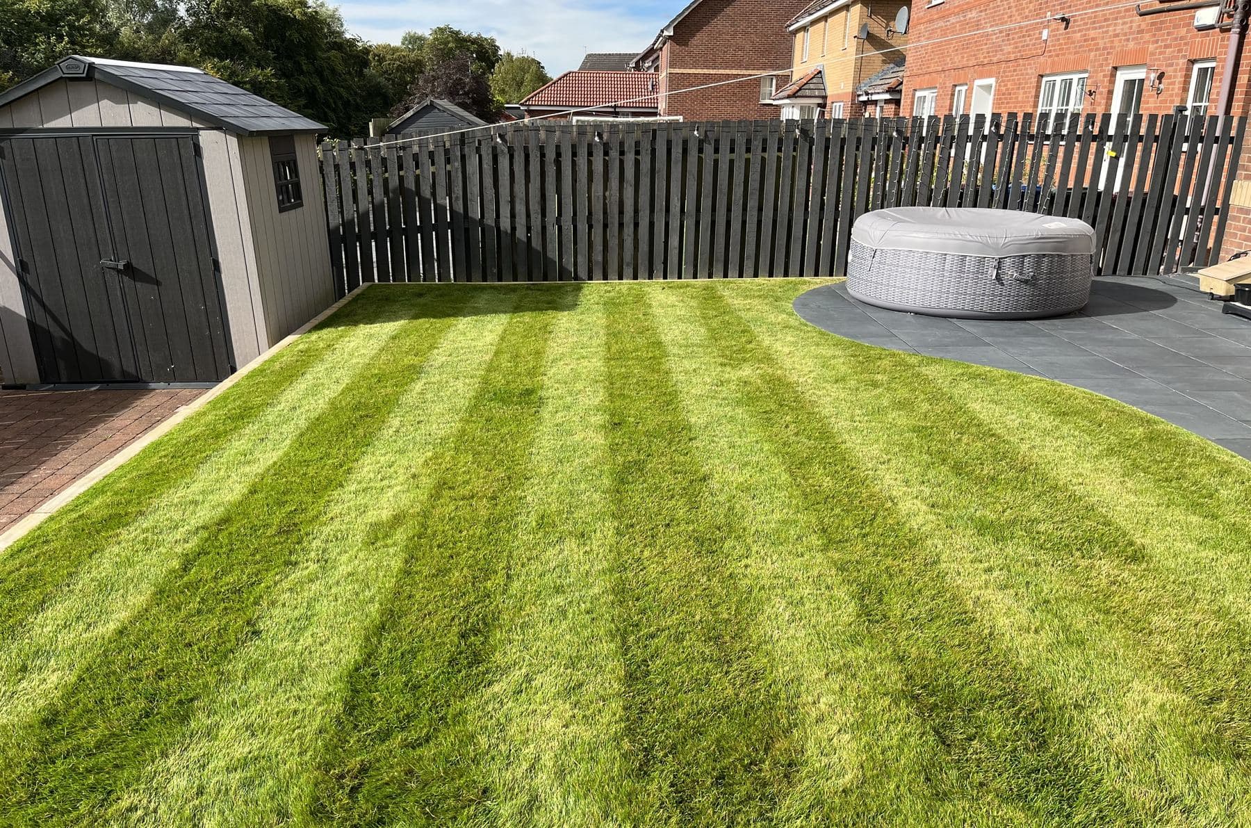 Wide striped rear lawn bordered by fencing and a paved seating area