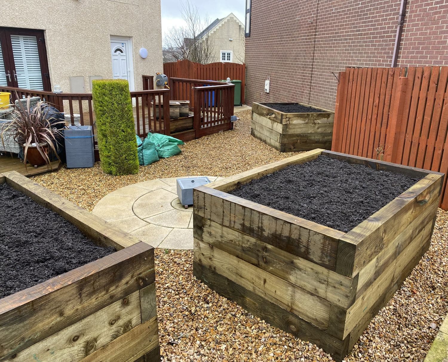 Newly built timber sleeper raised beds filled with compost on a gravelled patio