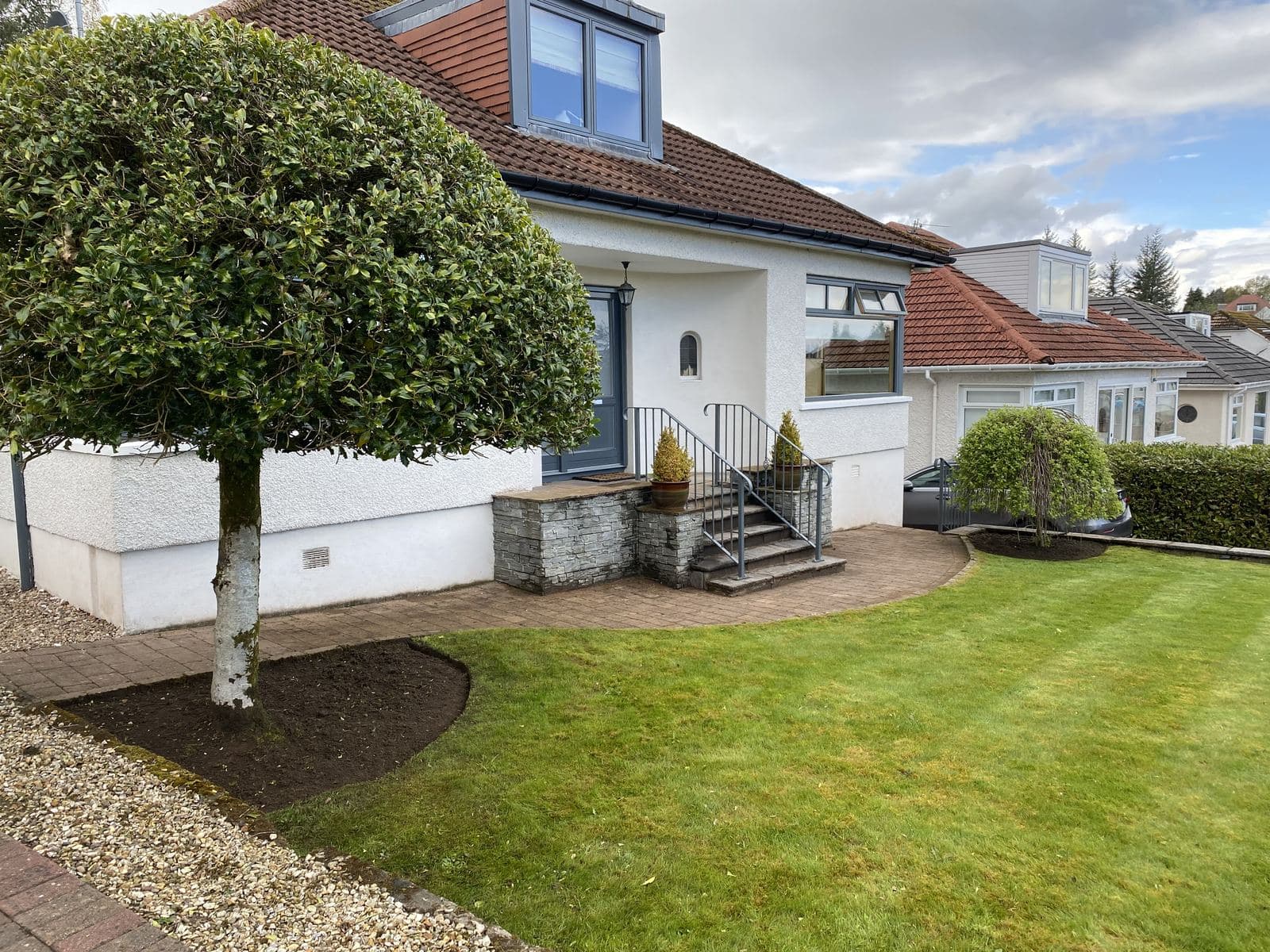 Clipped standard tree and edged lawn in the front garden of a white rendered house